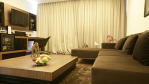 Una sala de estar moderna con una mesa de centro de madera, un sofá marrón, un televisor montado en la pared y un ventanal con cortinas.