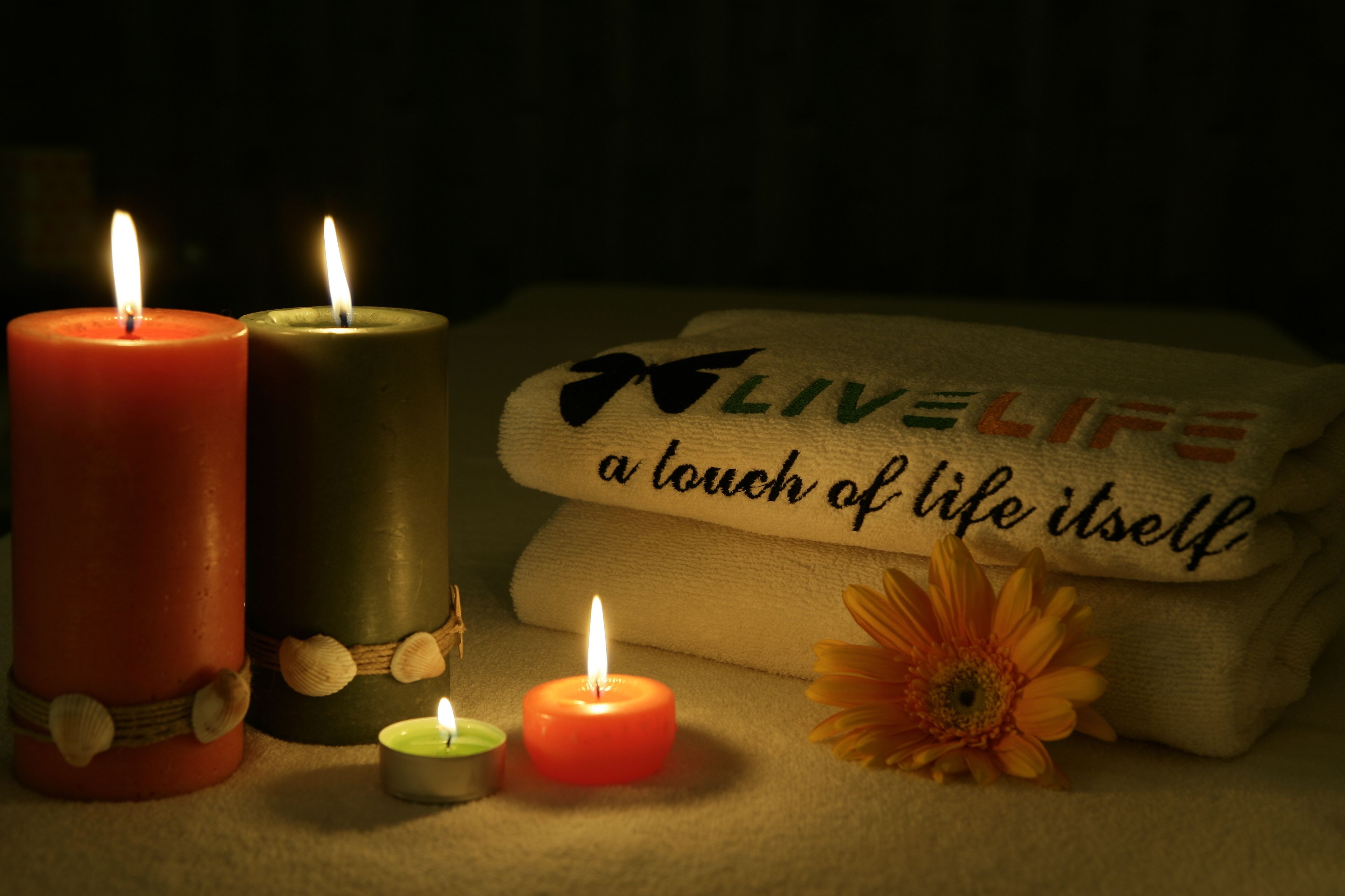 Tres velas encendidas, una toalla con el texto "Live Life a touch of life itself" y una flor.