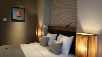 Una cama bien hecha con sábanas blancas y dos almohadas, una lámpara de pared y una obra enmarcada en la pared.