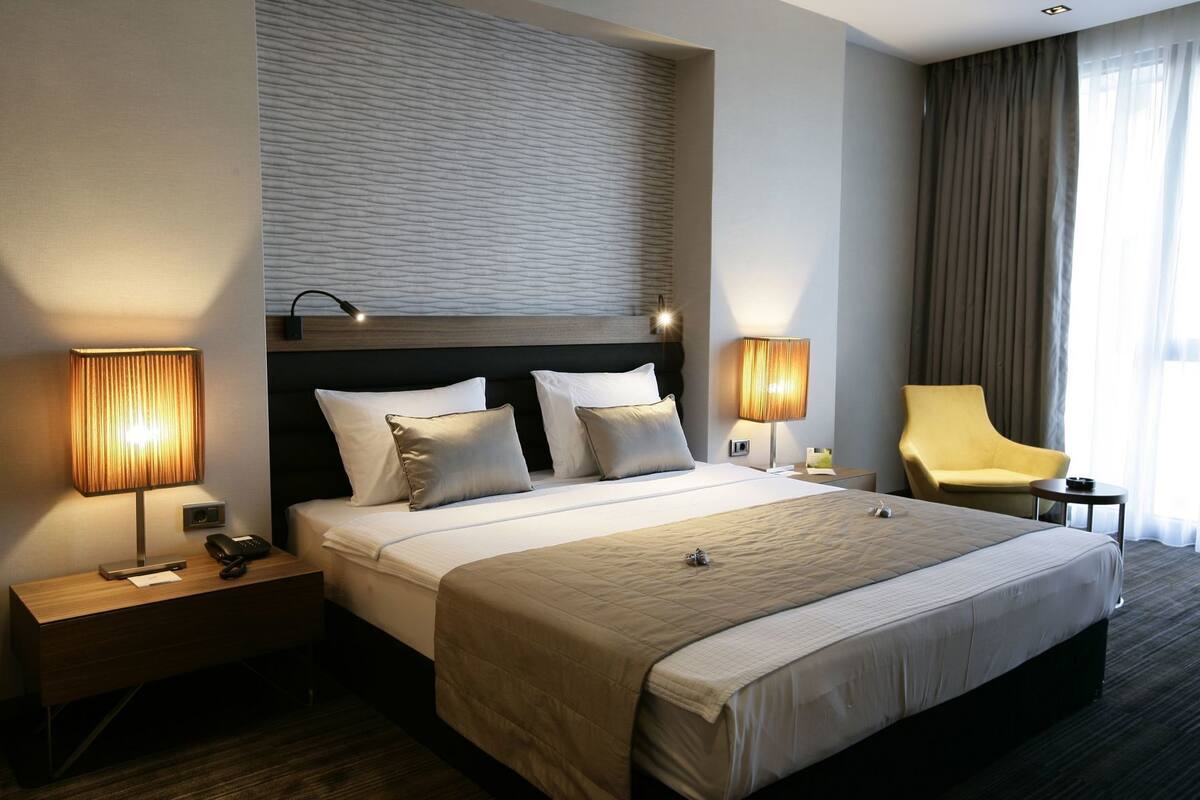 A hotel room with a large bed, two bedside tables, a chair, and a view of the outdoors.