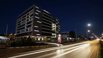 Un hotel de varios pisos con señalización iluminada, un estacionamiento y una calle bien iluminada de noche.
