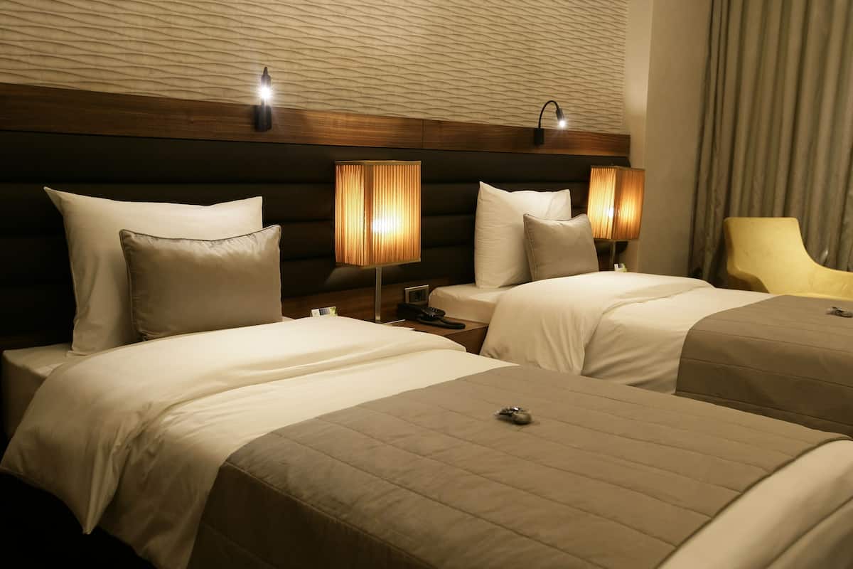 A hotel room with two beds, each with a pillow and a bedside lamp.