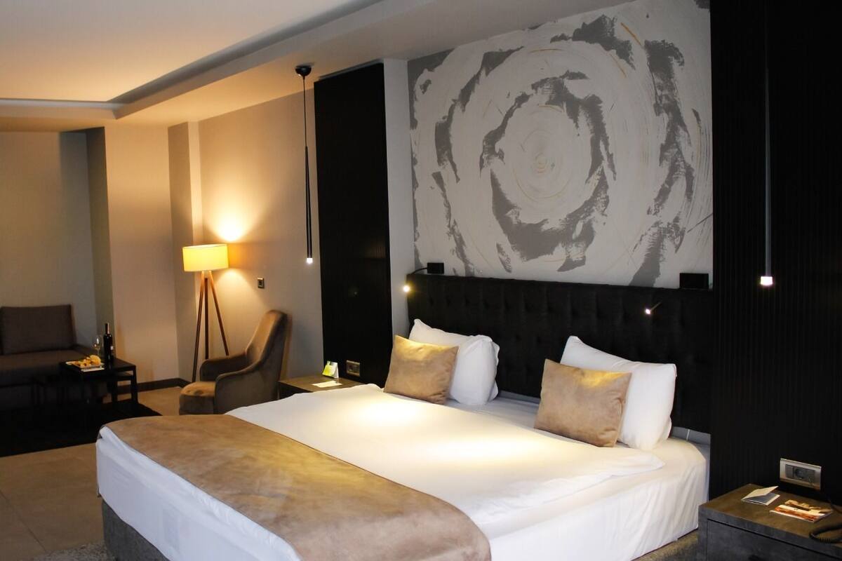 A modern hotel room with a large bed, a sofa, a chair, and a floor lamp.