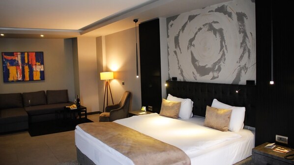 A modern hotel room with a large bed, a sofa, a chair, and a floor lamp.