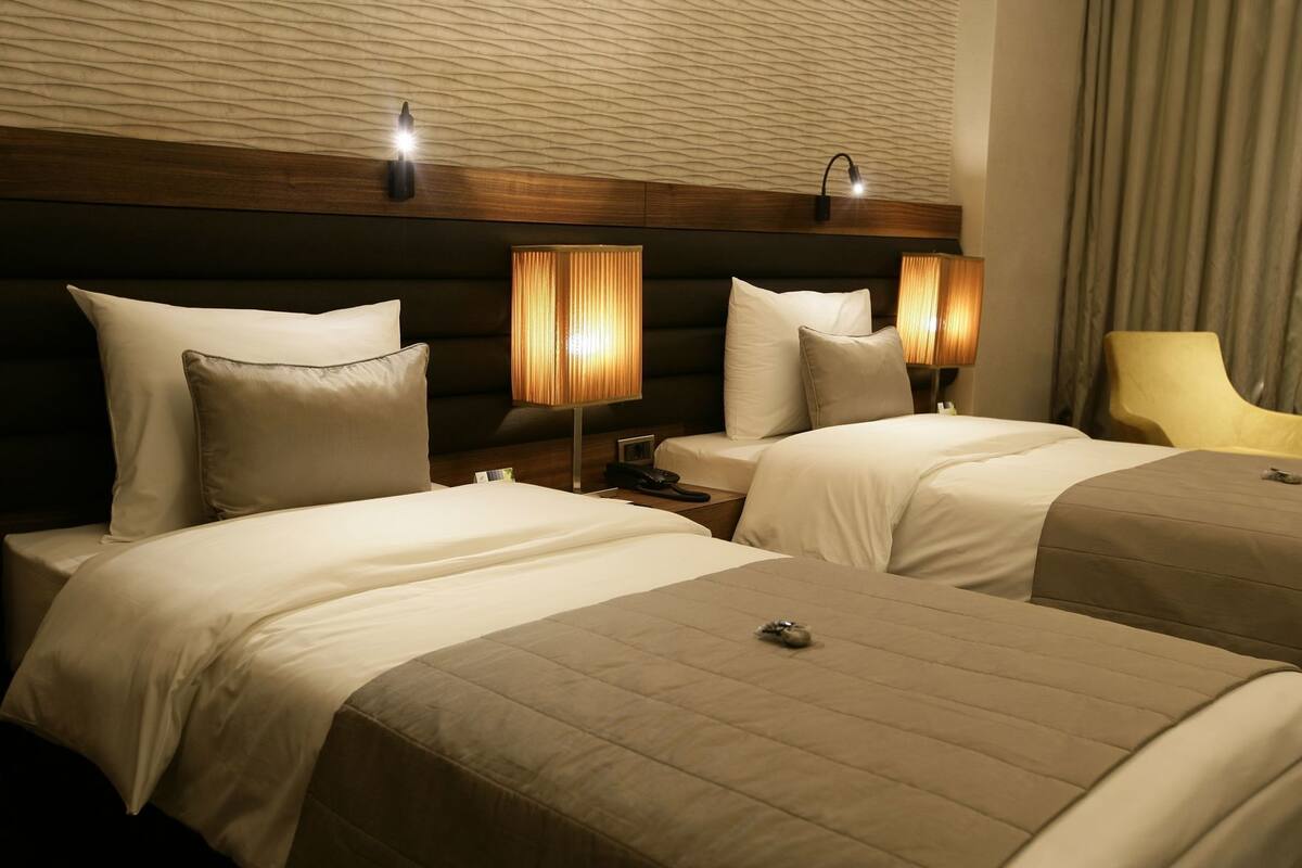 A hotel room with two beds, a wooden headboard, bedside lamps, a nightstand, and a chair.