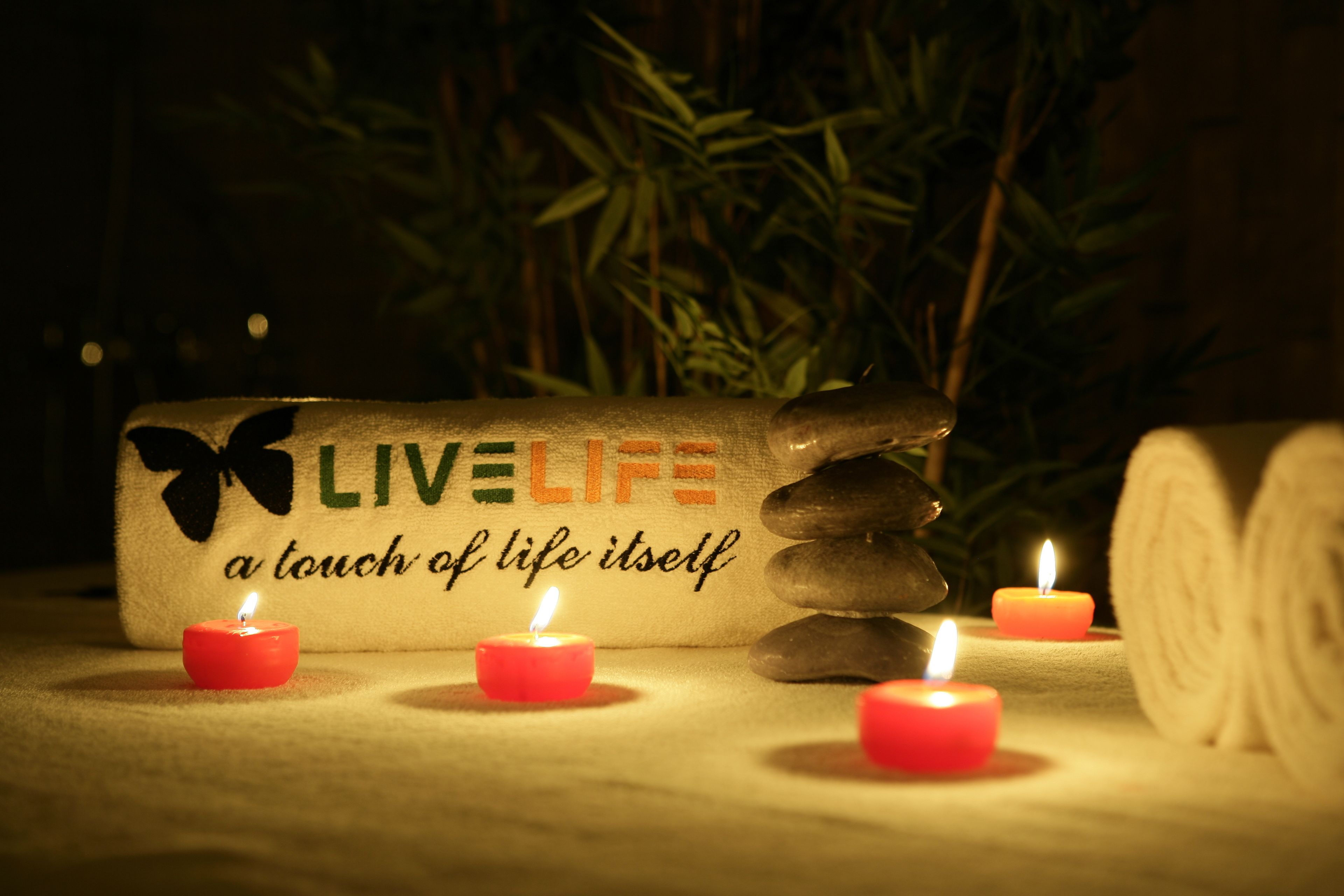 A serene setting with a massage stone, candles, and a towel with the text "LIVE LIFE a touch of life itself" in a dimly lit room.