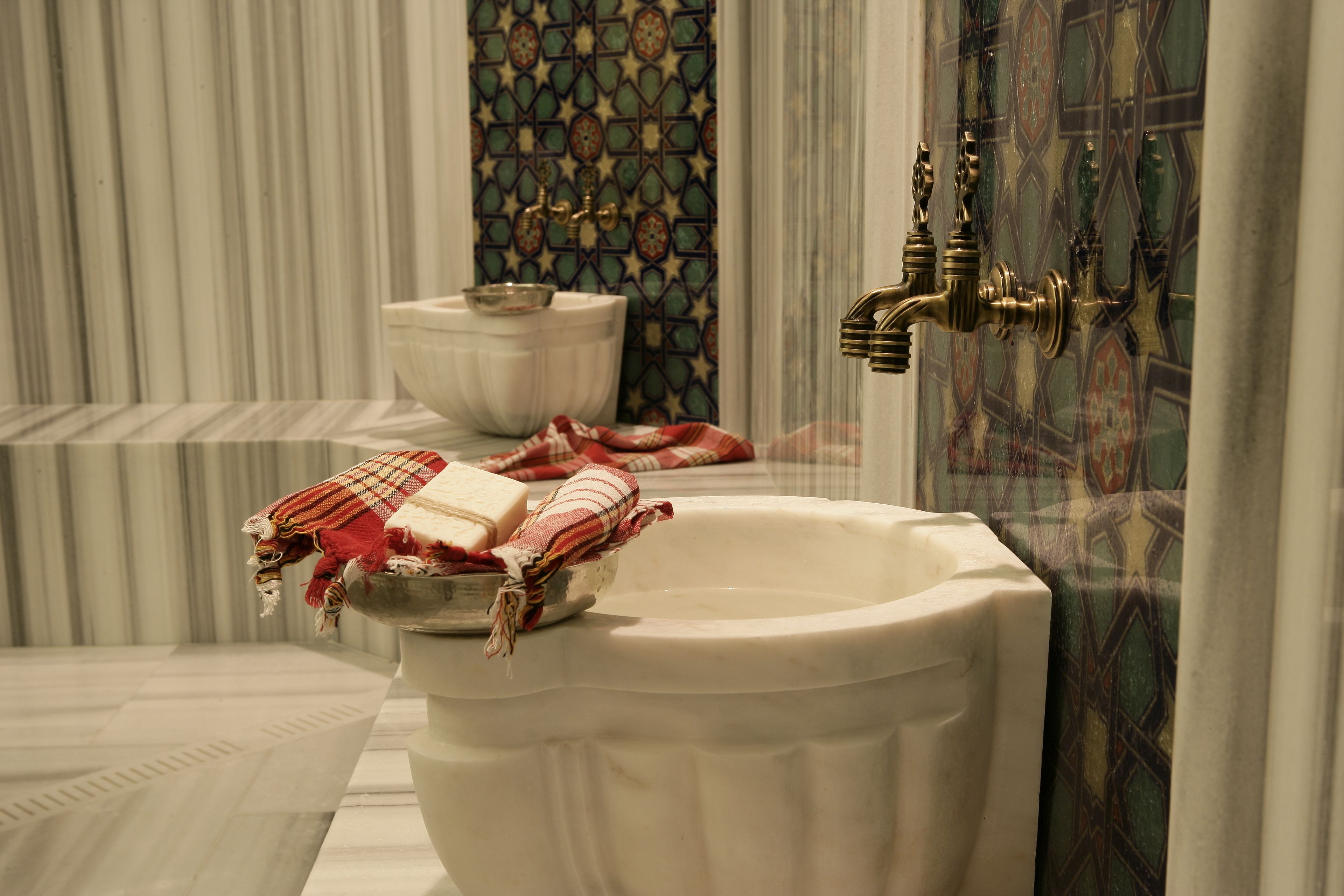 A bathroom with a white bathtub, a white toilet, and a decorative wall with a geometric tile pattern.