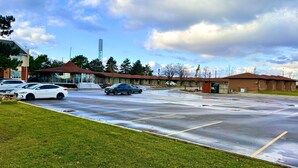 A parking lot with several cars, a building with a brown roof, and a tall structure in the background. - Vaughan Inn (Vaughan)