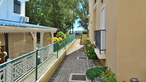 A narrow alleyway with a tiled walkway, a green fence, and buildings on either side.