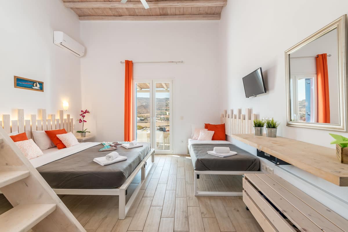 Una habitación de hotel moderna con dos camas, un televisor, un banco de madera, una mesita pequeña y un espejo grande.