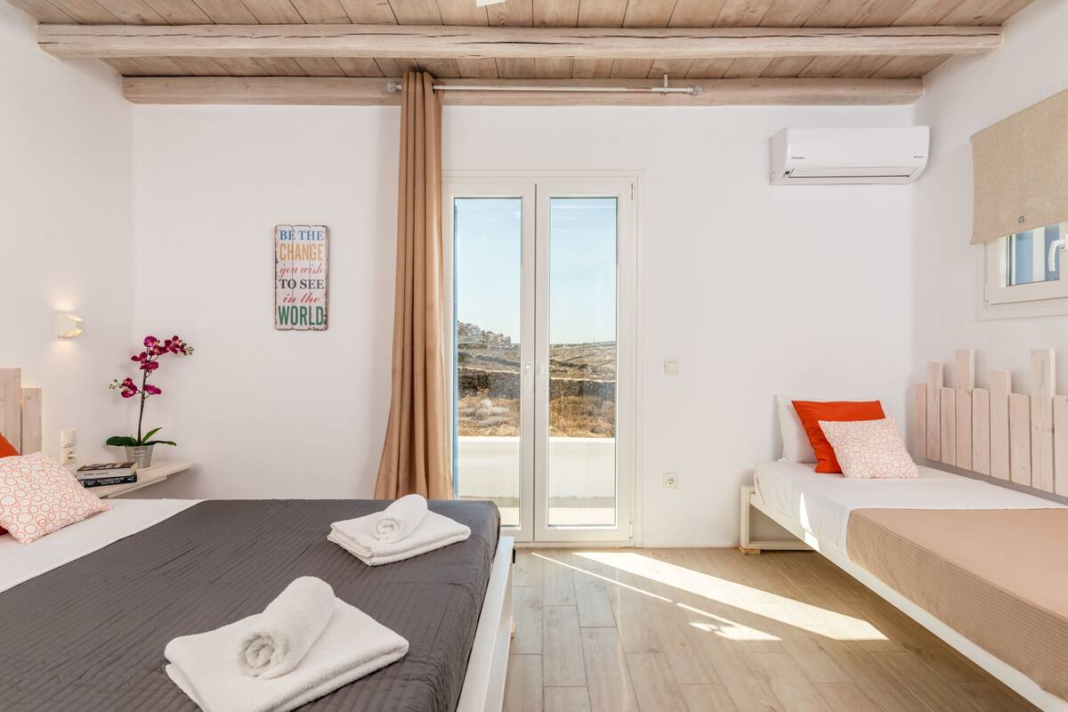 Un dormitorio con una cama, un banco, una planta en maceta y vistas a través de un ventanal.