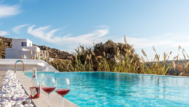 A pool with white pebbles, two glasses of red wine, and a bottle on the edge. - Electra Village (Mykonos)