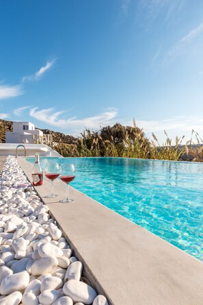 En pool med vita stenar, två glas rött vin och en flaska stående vid kanten.