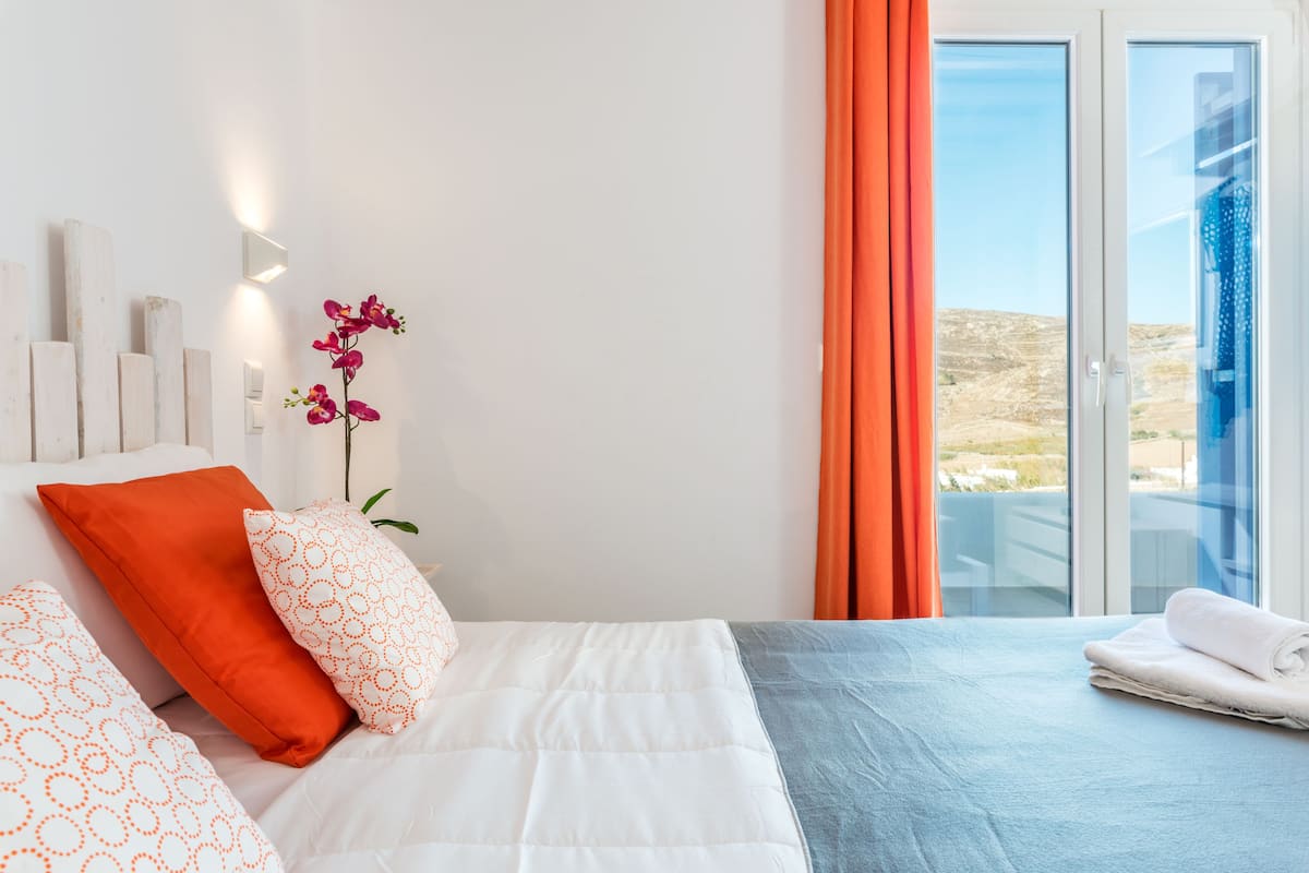 Una habitación de hotel moderna con cama, almohadas, una orquídea en maceta y vistas a través de una puerta de cristal.