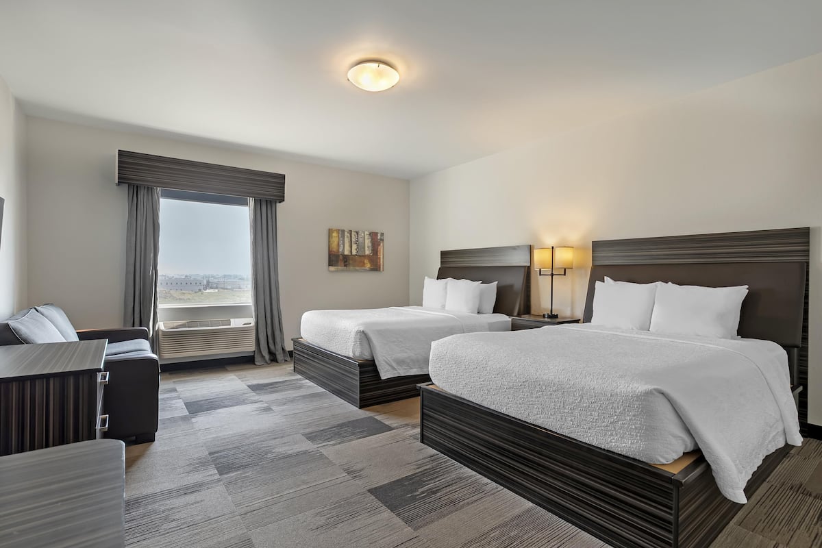 Habitación de hotel con dos camas, un escritorio, una silla y un amplio ventanal con cortinas.