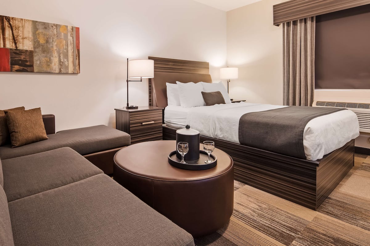 Habitación de hotel con cama, sofá, una mesita con un vaso y una taza, y un cuadro en la pared.