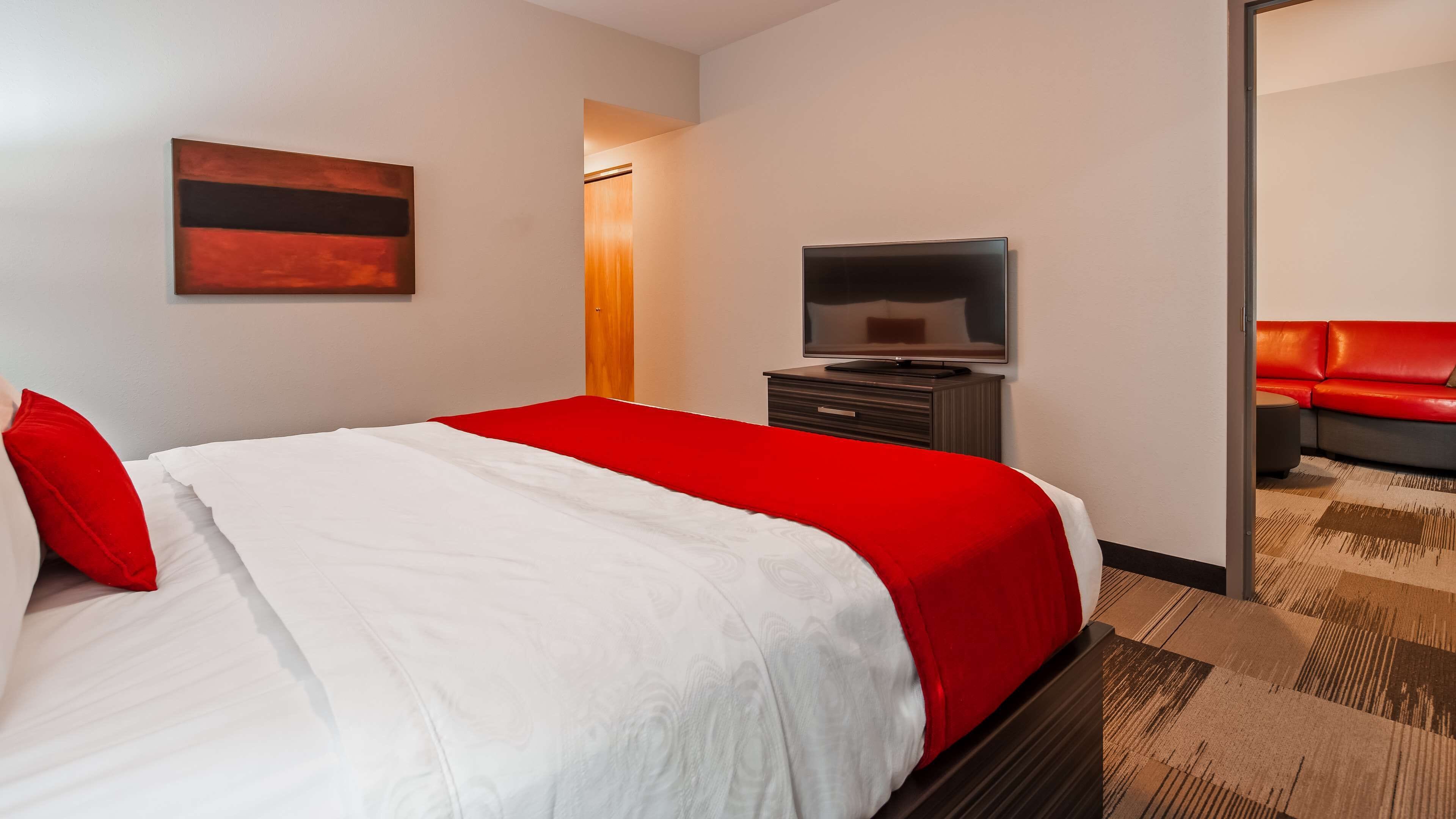 A hotel room with a bed, a TV, a red sofa, and a wooden cabinet.