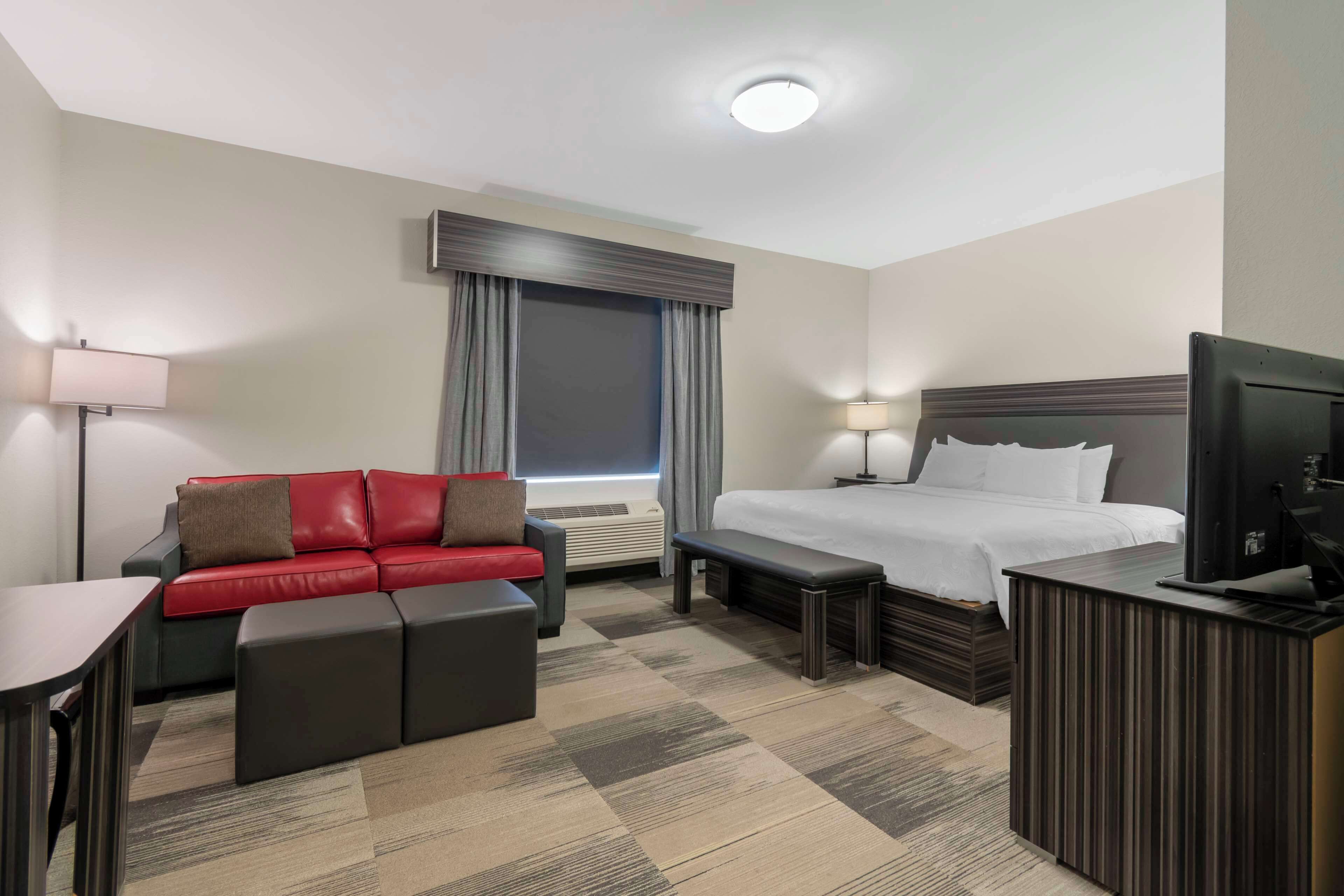 Una habitación de hotel con una cama, un sofá rojo, un escritorio y un televisor.