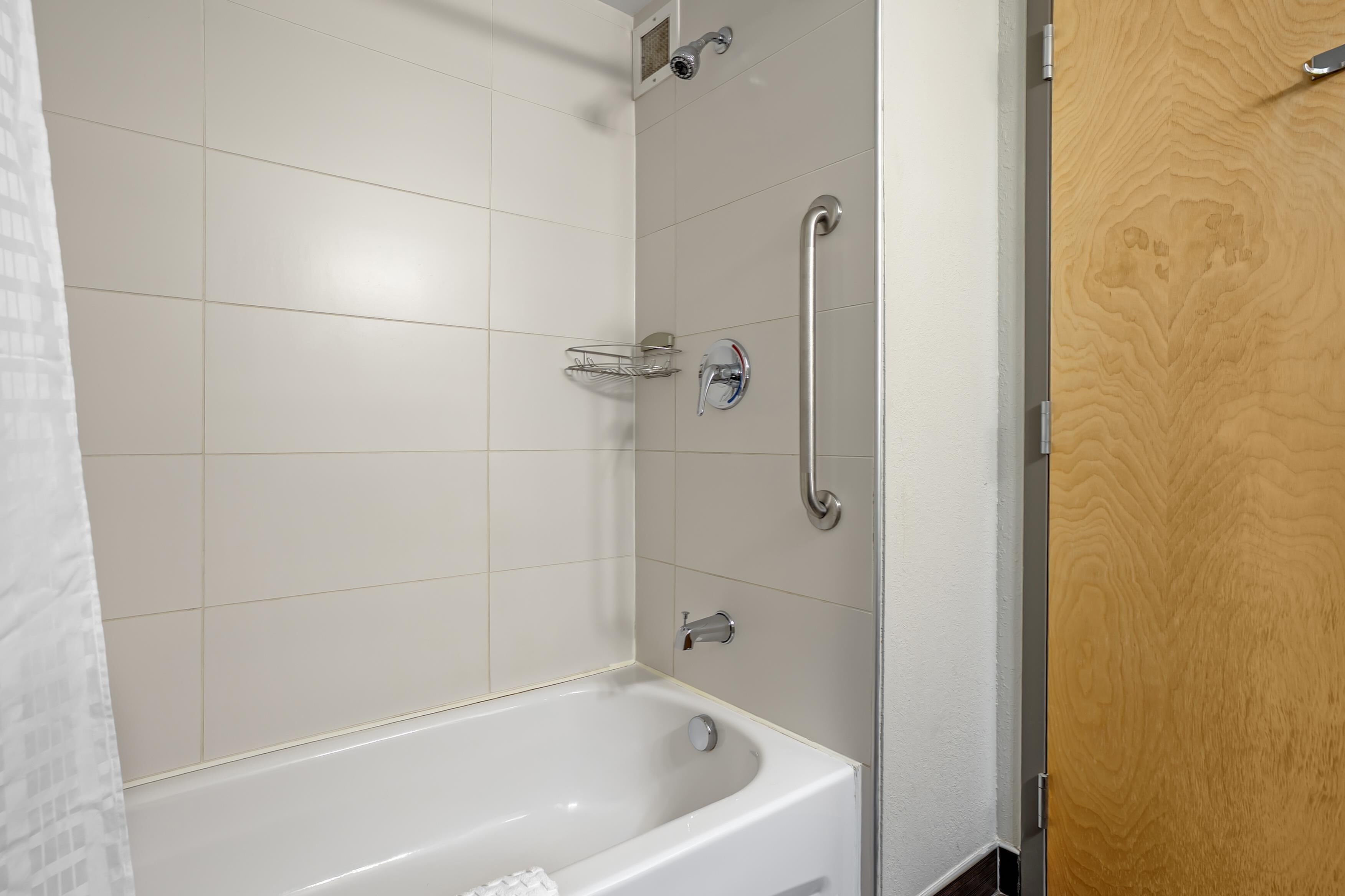 A bathroom with a white bathtub, a shower with a handheld showerhead, and a wooden door.