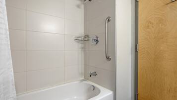 A bathroom with a white bathtub, a shower with a handheld showerhead, and a wooden door.