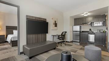 A modern hotel room with a bed, a seating area, a desk, and a kitchenette.