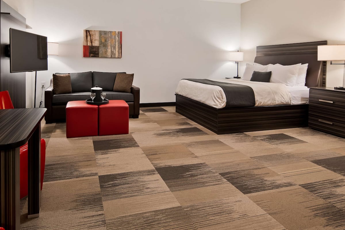 Una habitación de hotel con cama, sofá, televisión, mesa y un otoman rojo.
