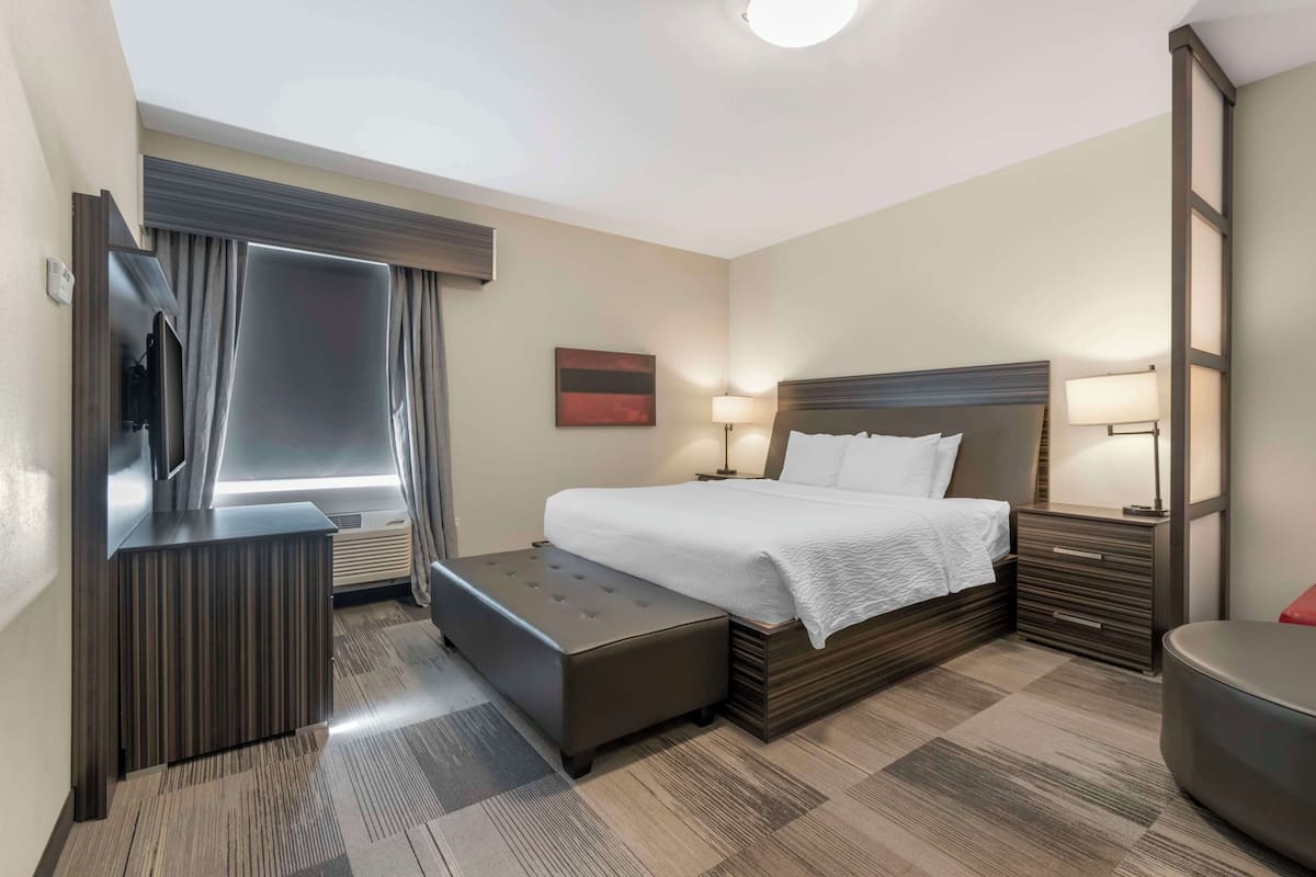 Habitación de hotel con cama, escritorio, silla, televisor y ventana con cortinas.