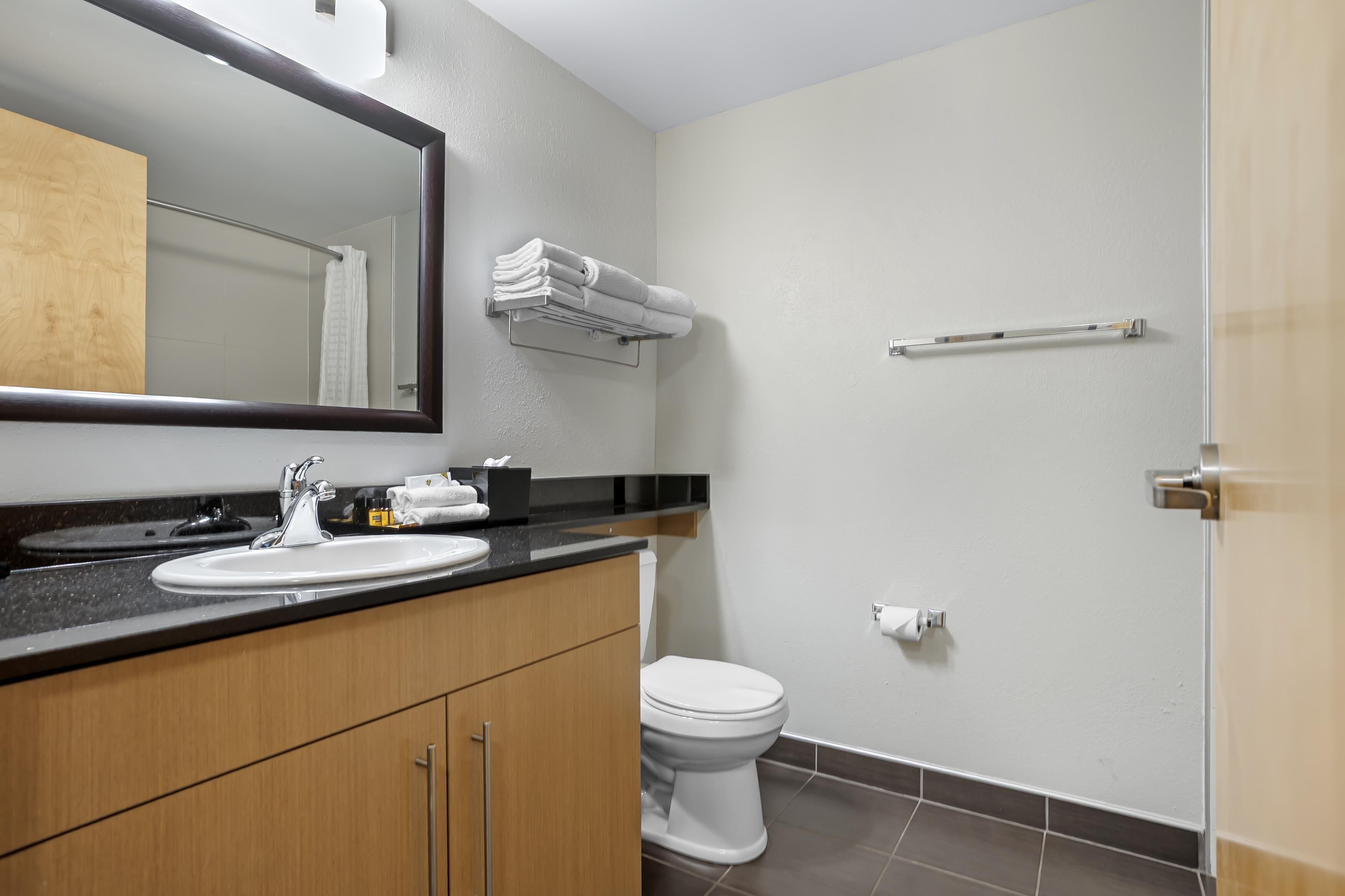 Un baño moderno con lavamanos, espejo, toallero, inodoro y zona de ducha.