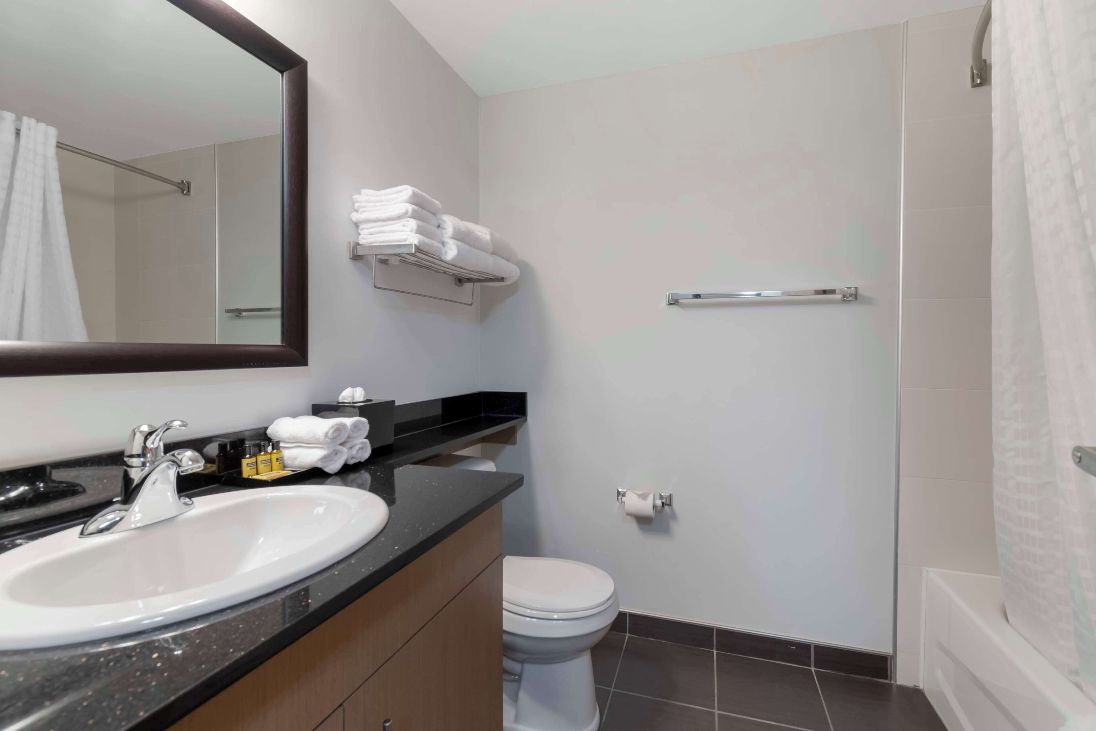 A modern bathroom with a sink, mirror, toilet, and shower area.