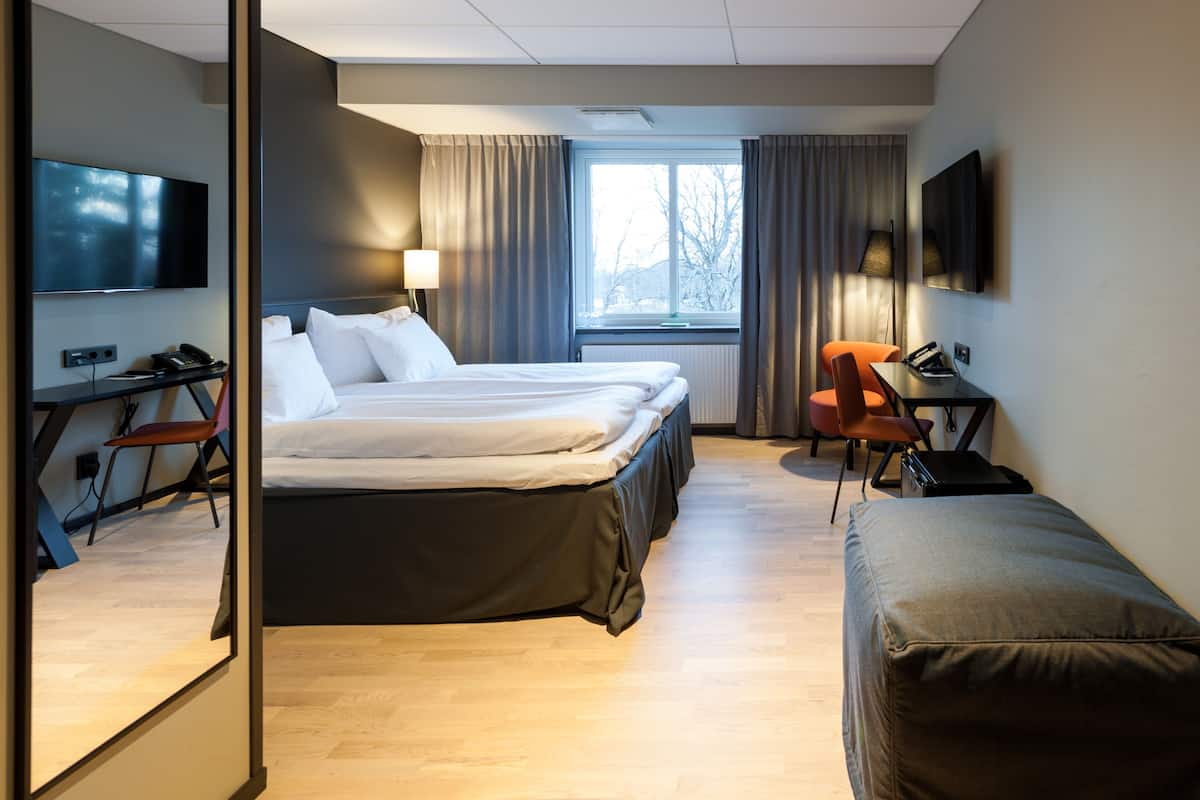 A hotel room with a bed, a desk, a chair, a TV, and a window with curtains.