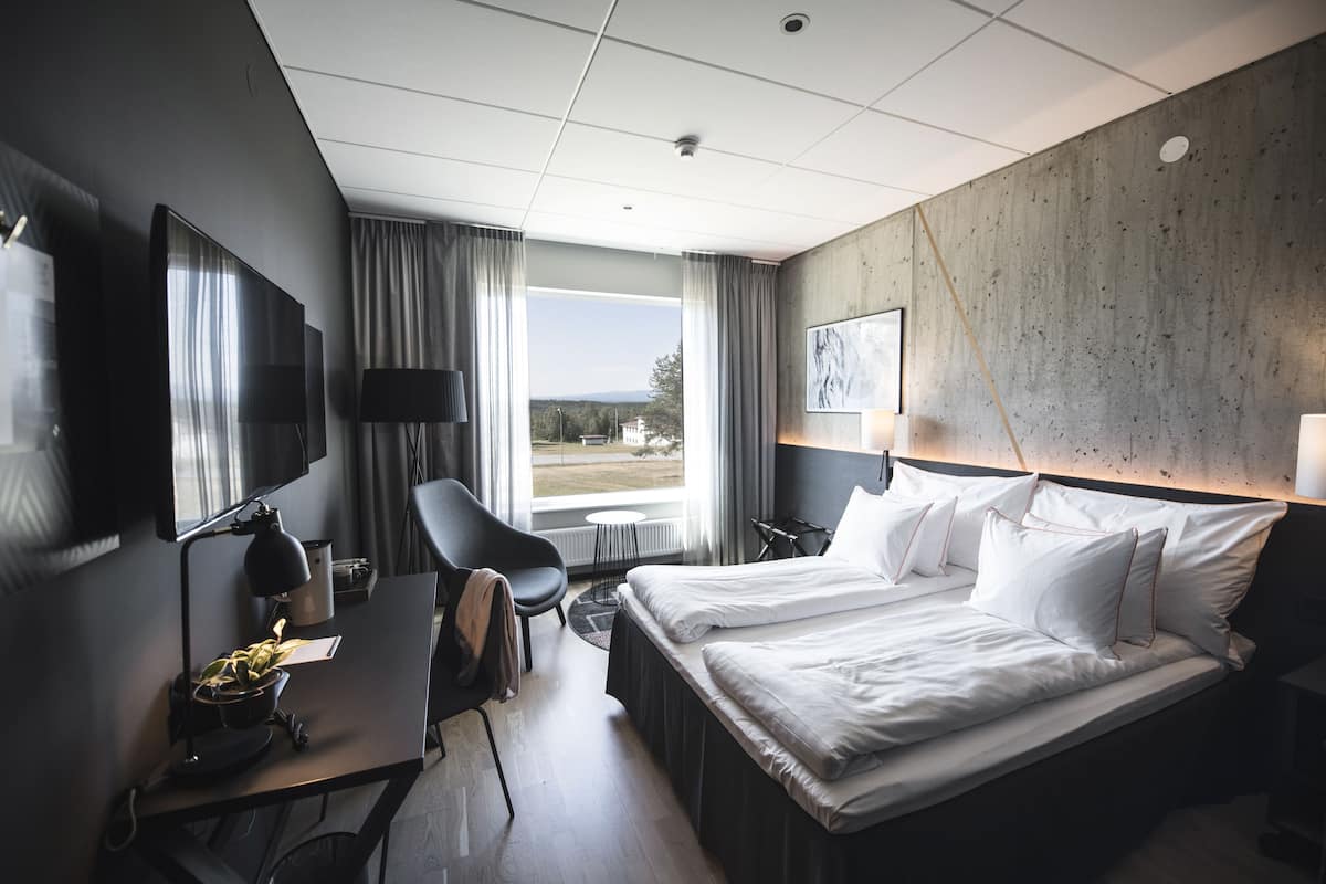A hotel room with a large bed, a desk with a lamp, a chair, and a view of the outdoors.