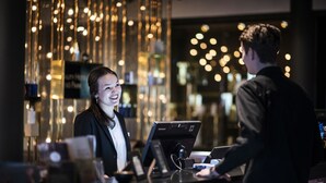 Un espace d’accueil d’hôtel au design moderne, comprenant un comptoir de réception équipé d’un ordinateur et d’une caisse enregistreuse.