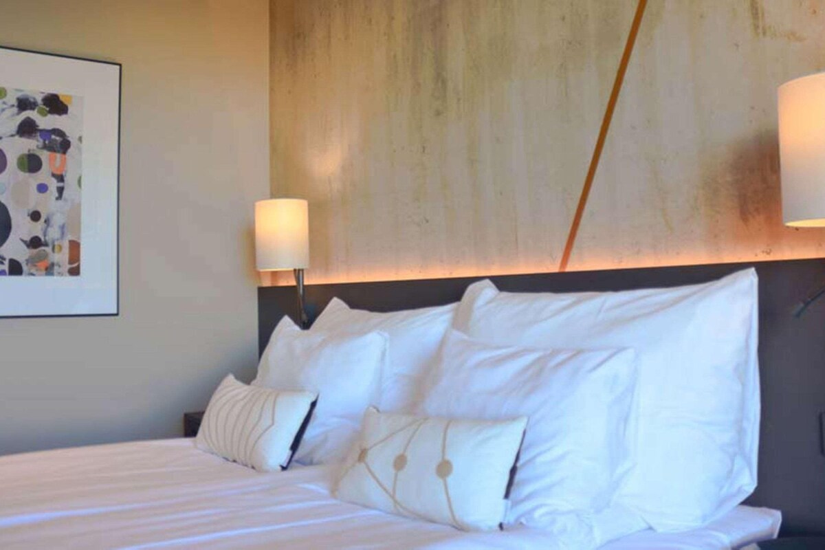 A hotel room with a large bed, a headboard, and a wall-mounted lamp.