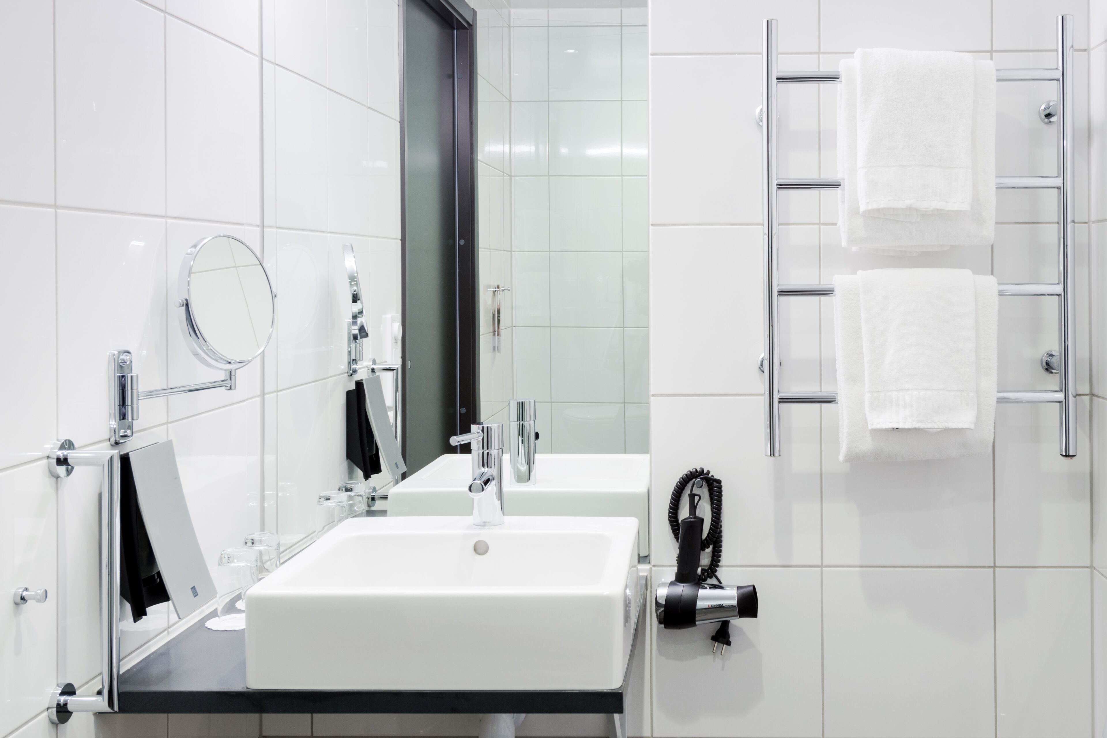 A modern bathroom with a large sink, a mirror, a towel rack, and a hairdryer.