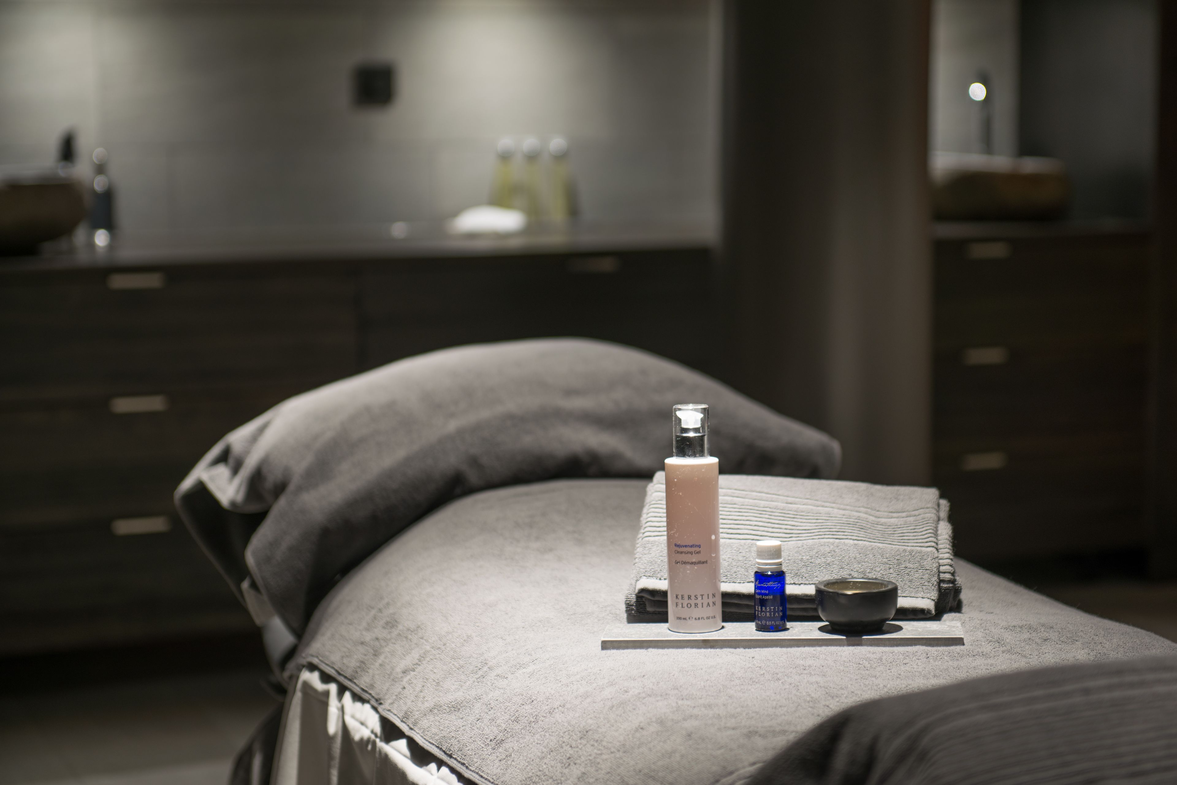 A neatly arranged bathroom with a towel, a bottle of shampoo, a bottle of lotion, and a small bowl on a counter.