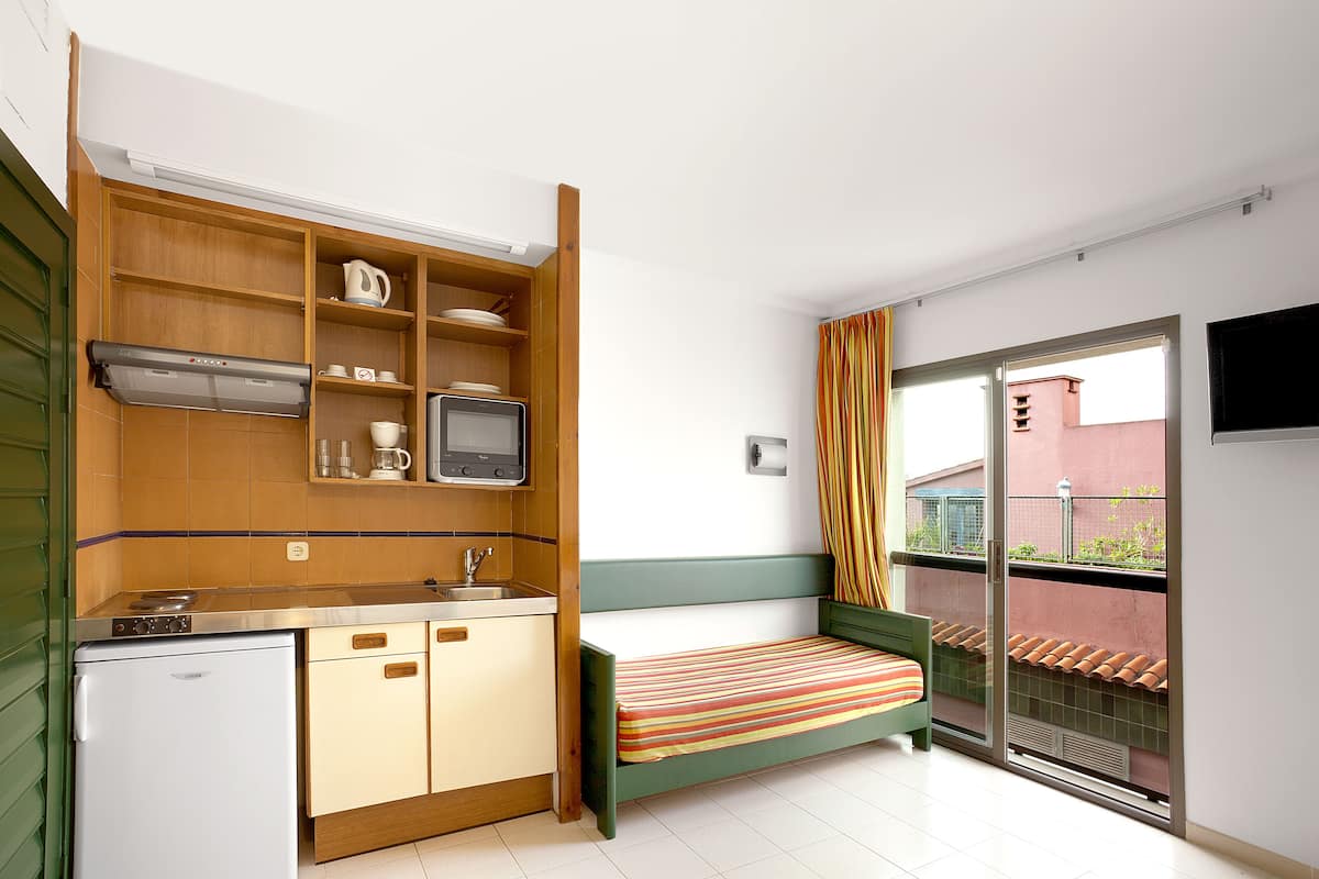 A compact room with a kitchenette, a bed, and a sliding glass door to a balcony.