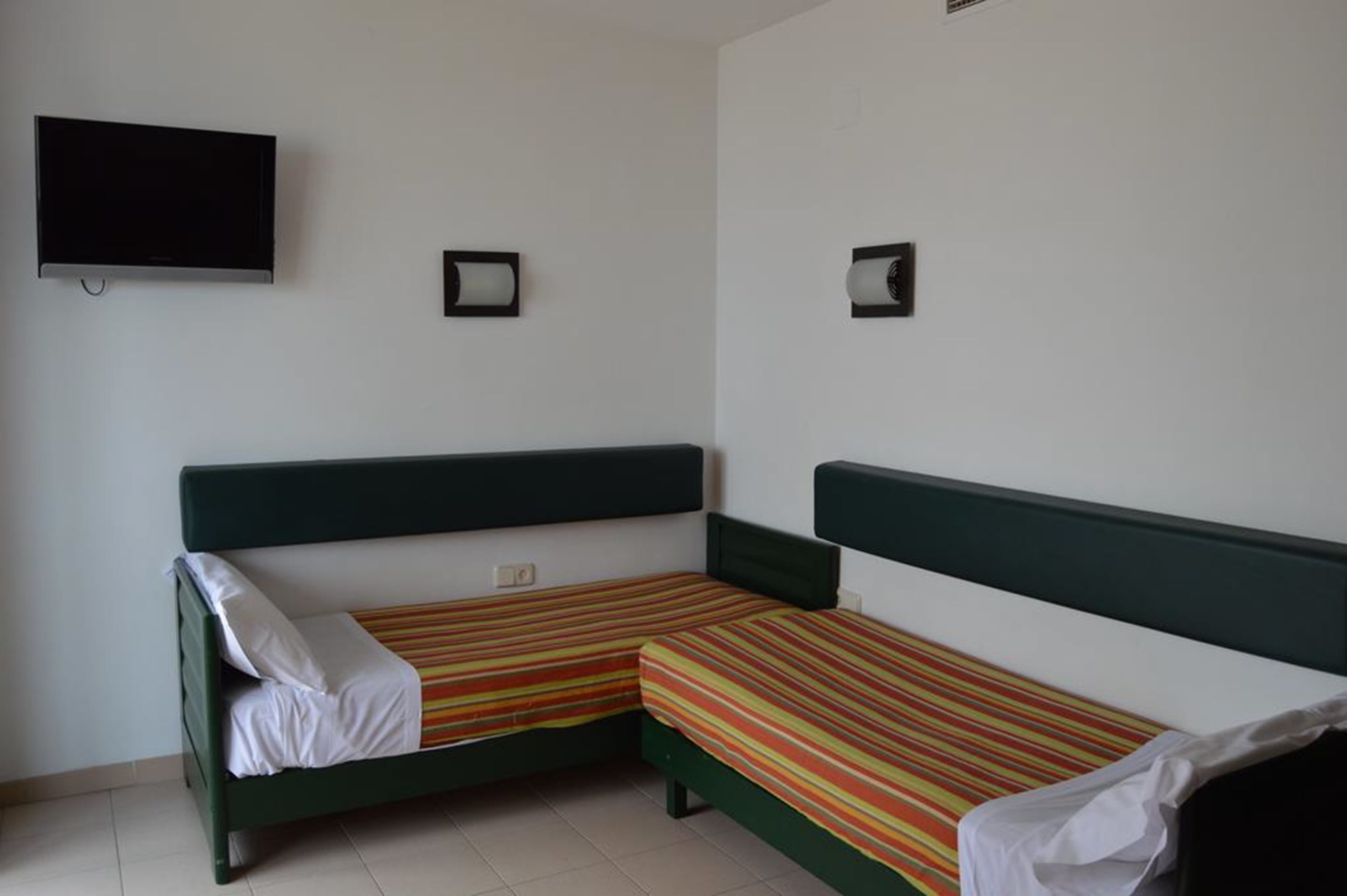 Una habitación con dos camas individuales, cada una con una colcha a rayas, un televisor montado en la pared y dos lámparas de pared.