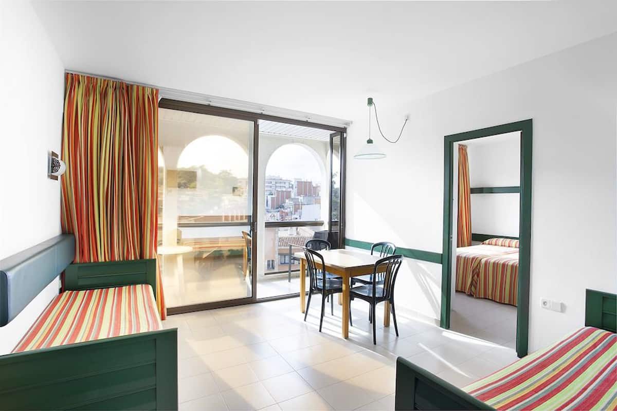A room with a bed, a table with chairs, a balcony with a view, and a sliding door.