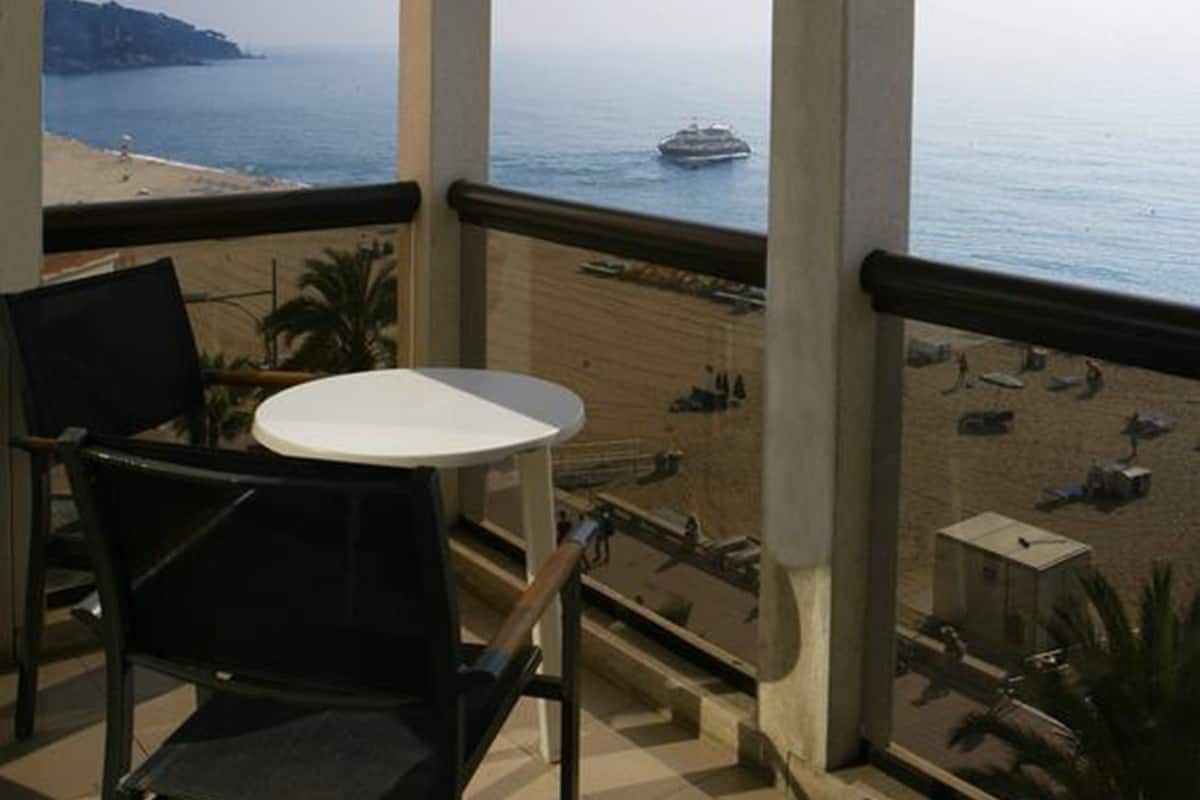 A balcony with a table and chairs, overlooking a beach with a boat in the distance.