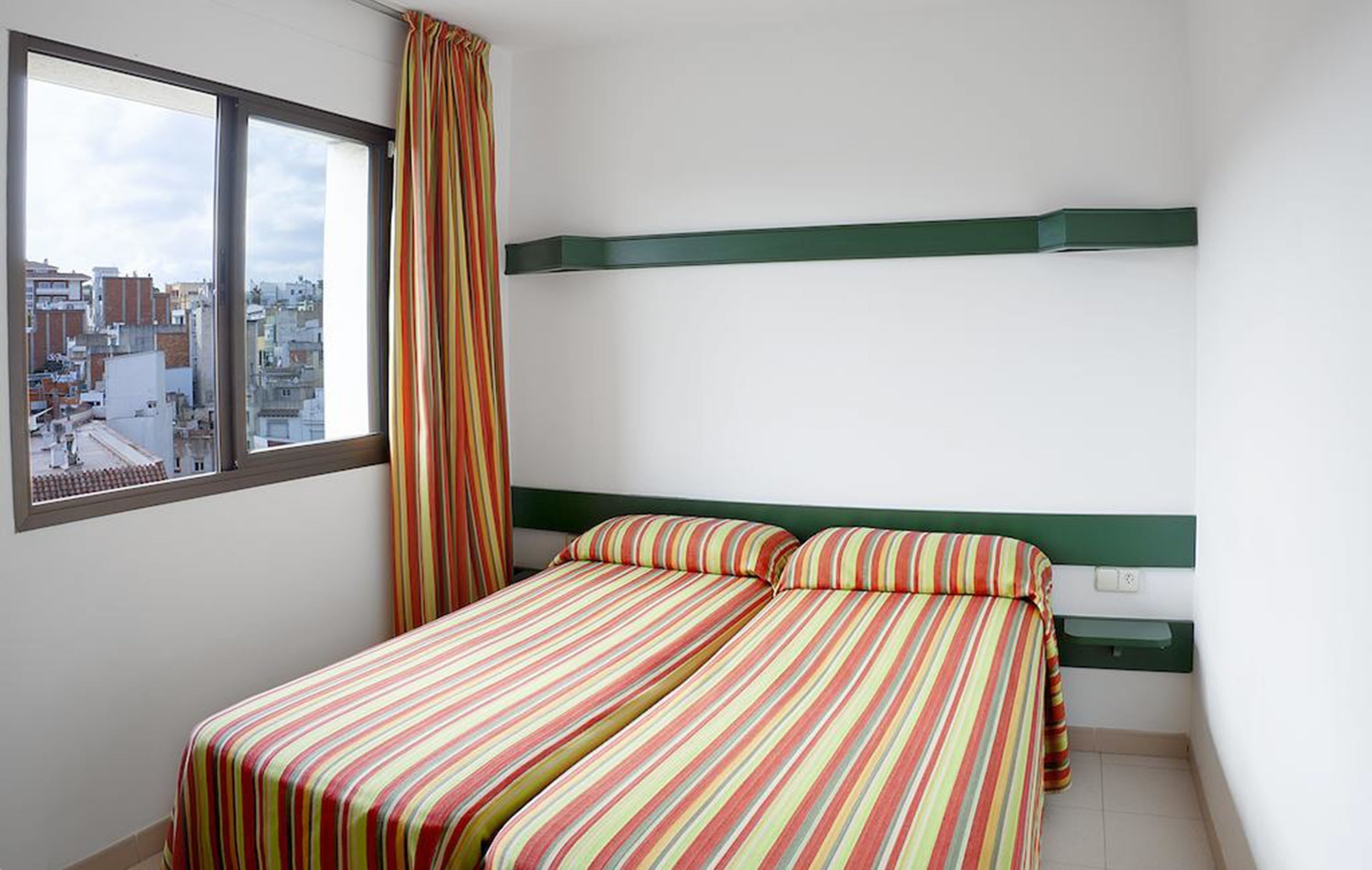 A room with a bed, a window, and a view of the city.