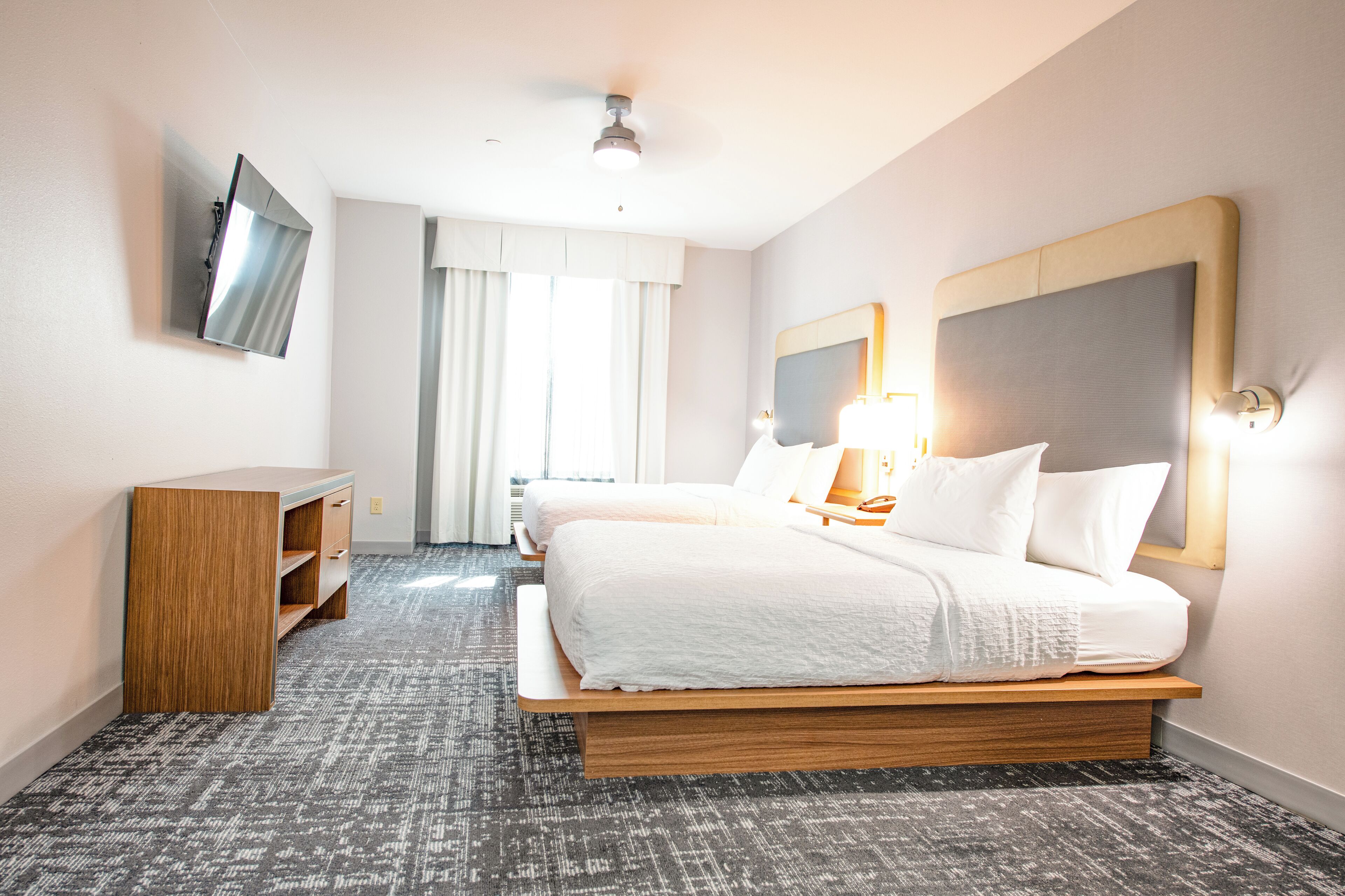 A hotel room with a large bed, a desk, a flat-screen TV mounted on the wall, and a ceiling fan.