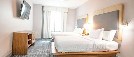 A hotel room with a large bed, a desk, a flat-screen TV mounted on the wall, and a ceiling fan.