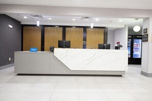 A hotel reception desk with a modern design, a check-in counter, and a cold beverage machine. - Homewood Suites Houma, La (Houma)