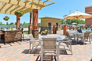 An outdoor patio area with tables and chairs, a pool, and a view of a body of water. - Homewood Suites Houma, La (Houma)