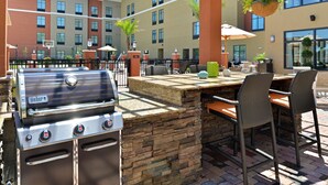 An outdoor patio with a Weber grill, wicker chairs, and a stone countertop. - Homewood Suites Houma, La (Houma)