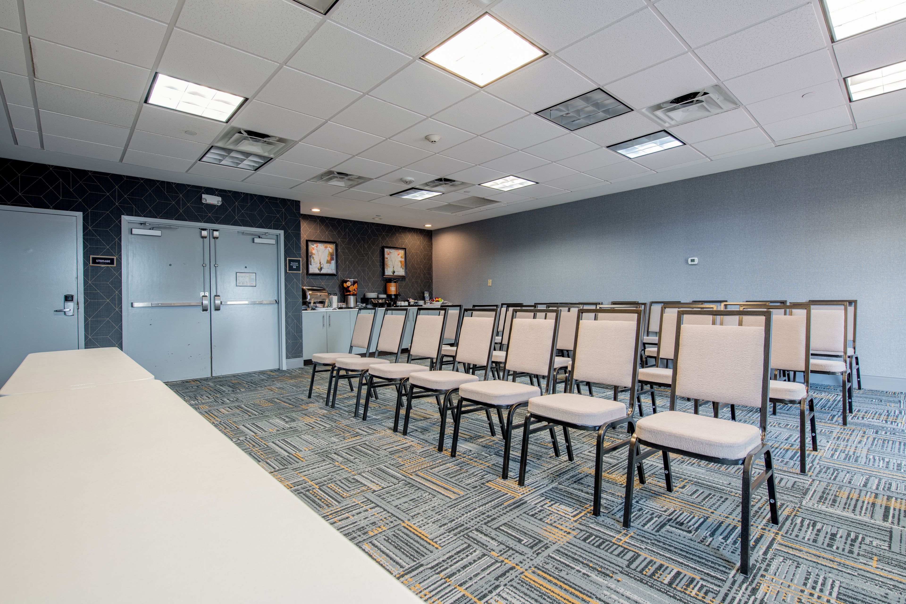 Ein Konferenzraum mit einem langen Tisch, Reihen von Stühlen, einer Küchenzeile und Stauraumschränken.
