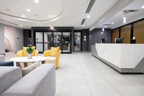 A modern reception area with a white reception desk, seating with yellow cushions, and a glass door entrance. - Homewood Suites Houma, La (Houma)