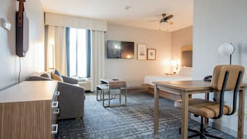 A hotel room with a bed, a desk, a chair, a TV, and a ceiling fan.