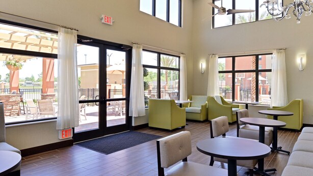 A spacious indoor seating area with multiple tables and chairs, large windows with curtains, and an exit sign. - Homewood Suites Houma, La (Houma)