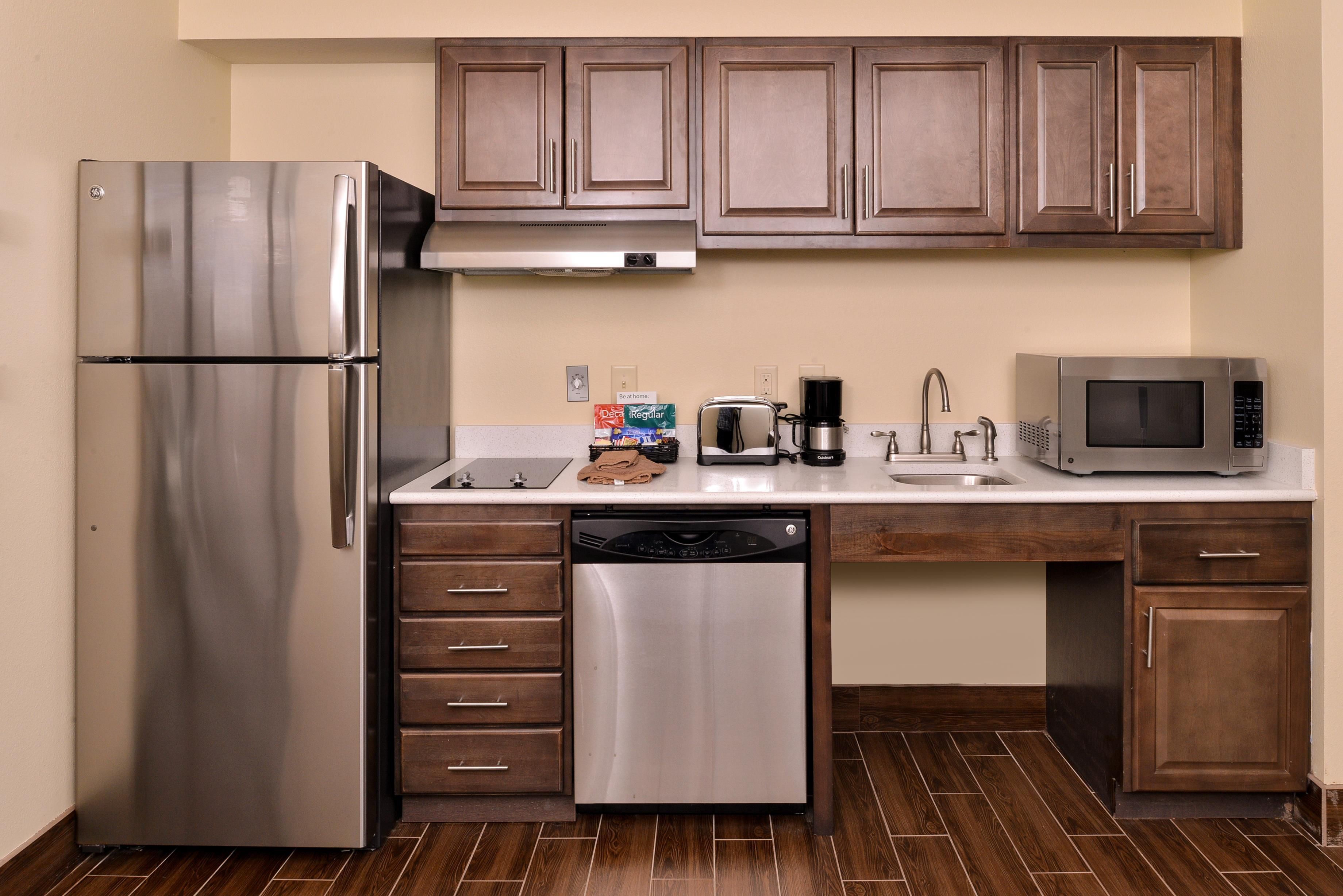 A kitchen with a stainless steel refrigerator, a dishwasher, a microwave, and wooden cabinets.